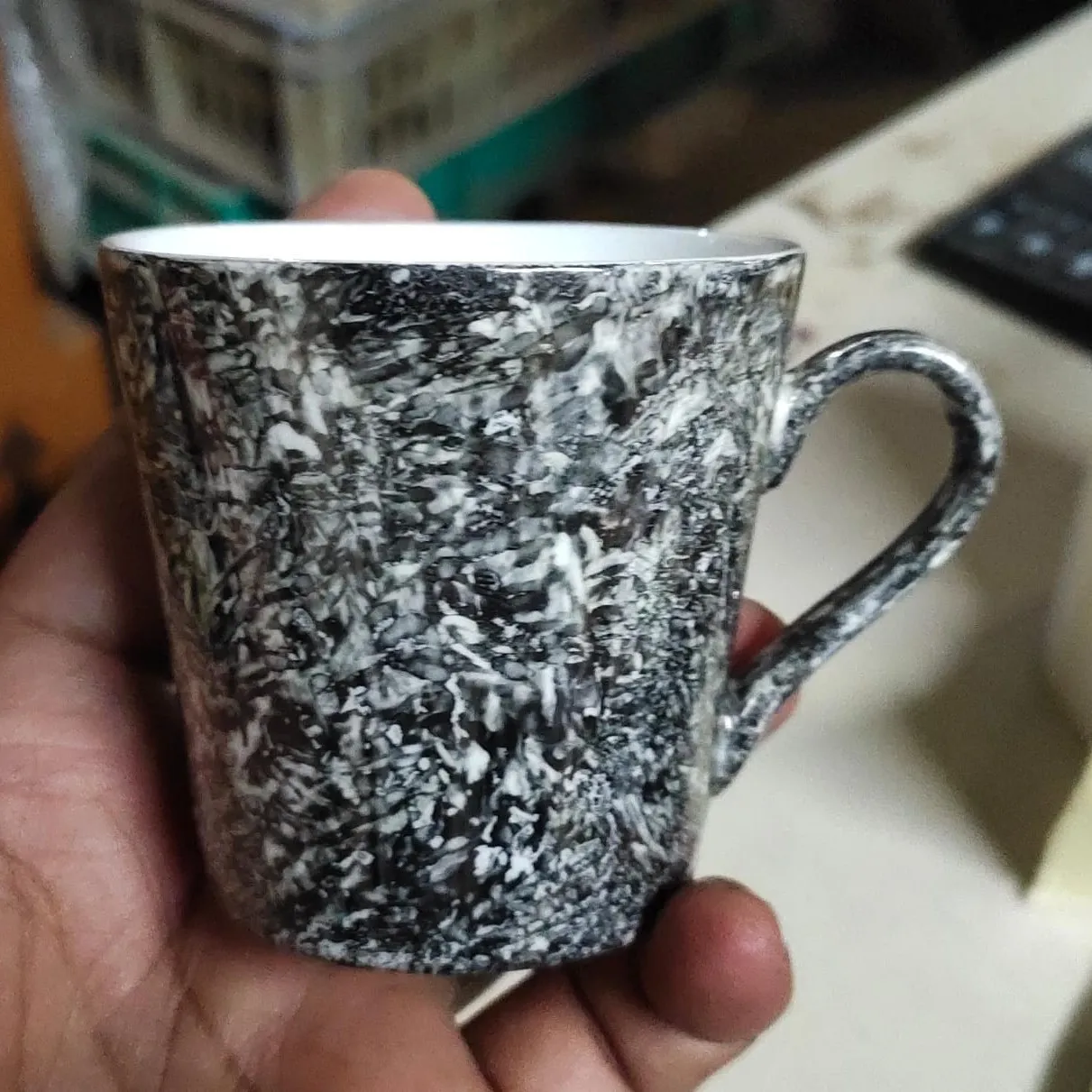 A mug decorated with black lustre, held in a hand